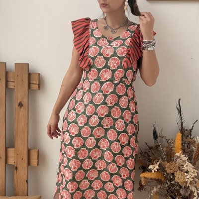 Vestido midi estampado com padrão de conchas cor-de-rosa e verde com folhos às riscas, usado com acessórios metálicos e sapatilhas com purpurina.