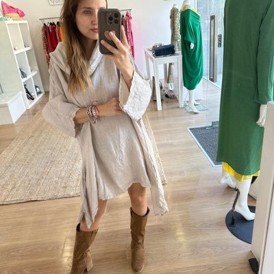 Mulher a tirar selfie vestindo vestido cinzento claro e botas castanhas numa loja com manequins e roupa ao fundo