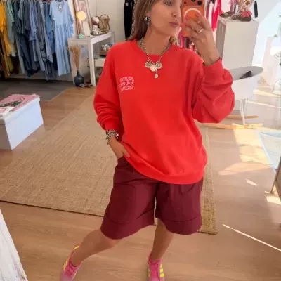 Mulher a tirar selfie na loja com sweat vermelho, calções vinhos e ténis rosa e amarelo