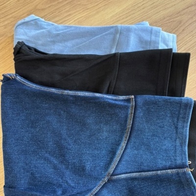 Três pares de calças dobradas em diferentes cores sobre uma mesa de madeira.