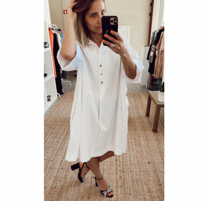 Mulher a usar vestido branco com botões e sandálias pretas junto a espelho