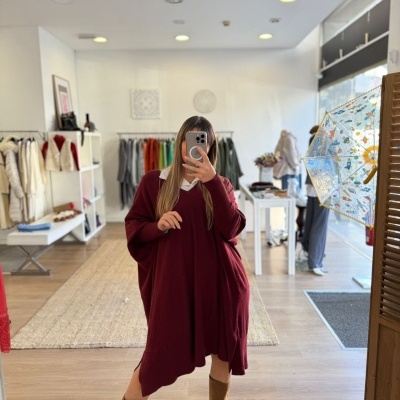 Mulher com vestido oversized bordô e botas camel numa loja de roupa
