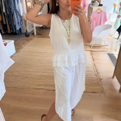 Mulher a tirar selfie veste conjunto branco e acessórios, loja ao fundo