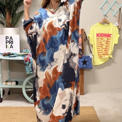Mulher com vestido comprido colorido em azul, castanho, bege e branco com padrão abstrato, em interior decorado.