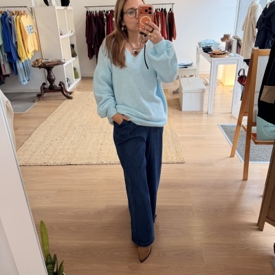 Mulher com camisola azul e calças de ganga em loja de roupa a tirar selfie no espelho