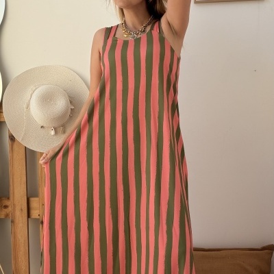 Vestido comprido com riscas verticais rosa e verde, comentado por mulher com acessórios e chapéu de palha ao fundo.