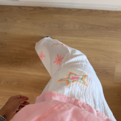 Pantalonas brancas bordadas coloridas e t-shirt rosa em chão de madeira