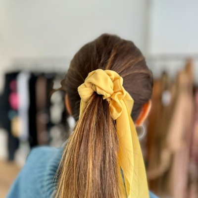 Elástico de cabelo amarelo com fita adjacente num rabo de cavalo castanho claro