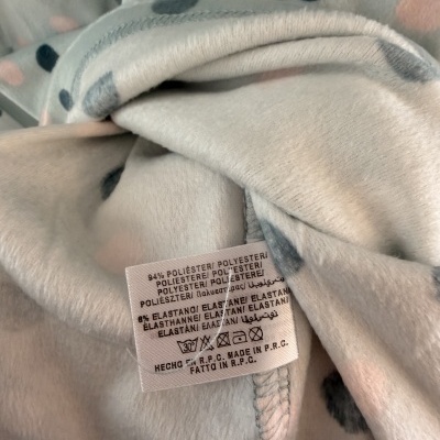 Tecido cinza claro com bolinhas e etiqueta de composição em poliéster e elastano