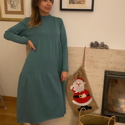 Mulher com vestido verde-azulado junto a lareira com decoração natalícia.
