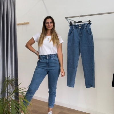 Calças de ganga azuis com cintura subida e elástica em exposição com modelo e penduradas numa barra, fundo branco e planta verde.