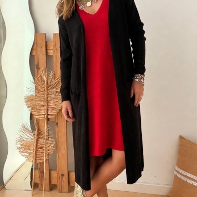 Mulher com vestido vermelho e casaco preto em ambiente interior com chão de madeira.