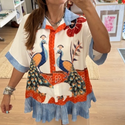 Camisa com padrão de pavões e calças largas bege num ambiente de loja de roupas.