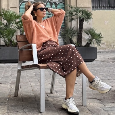 Mulher sentada numa cadeira em rua de pedra usando roupa casual em tons castanhos e laranja