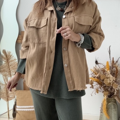 Mulher com casaco bege e conjunto verde escuro em ambiente minimalista.