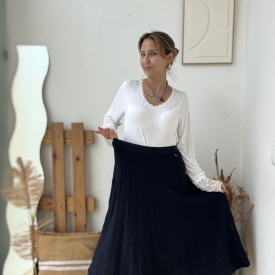 Mulher com blusa branca de manga comprida e saia preta plissada num ambiente decorado minimalista