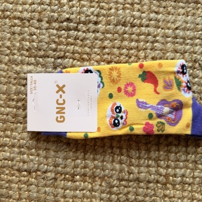 Meias amarelas e roxas com caveiras mexicanas e flores, embalagem com etiqueta GNC-X.