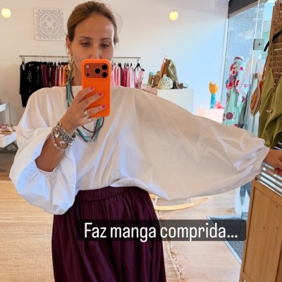 Mulher a tirar selfie com camisola branca de manga comprida e saia vinho numa loja de roupas.