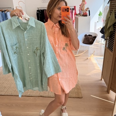 Mulher com camisa laranja e camisa verde claro bordada segurada em loja de roupa