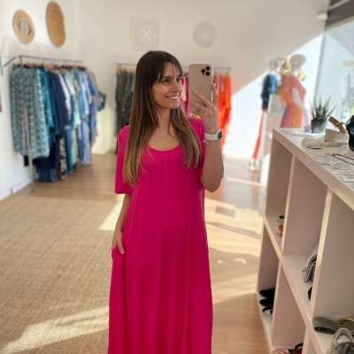 Mulher de vestido rosa fúcsia longo a tirar selfie numa loja de roupa.