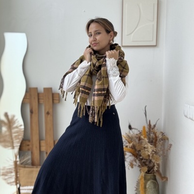 Mulher com saia preta canelada, blusa branca de renda e xale xadrez castanho e verde com franjas