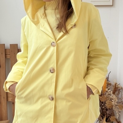 Casaco amarelo com capuz e botões usado por pessoa em ambiente interior com decoração