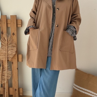 Mulher com casaco bege, camisa xadrez, calças de ganga largas e botins castanhos em ambiente interior
