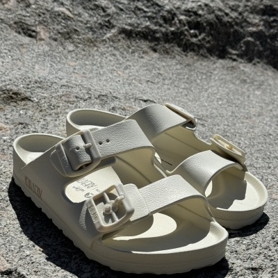 Sandálias brancas com duas tiras largas e fivelas sobre superfície de pedra cinzenta