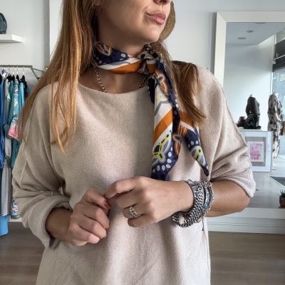 Mulher com cachecol colorido e camisola bege numa loja de roupa