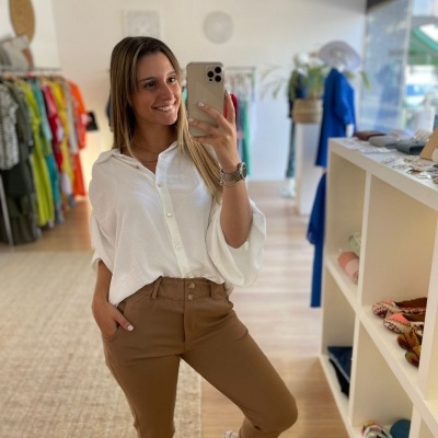 Mulher a tirar selfie numa loja de roupa, vestindo camisa branca e calças castanhas