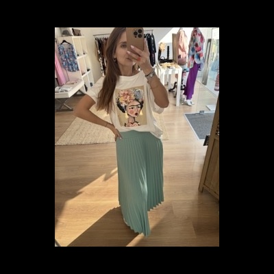 Pessoa com t-shirt branca e saia plissada verde-água a tirar selfie em espelho em loja de roupa