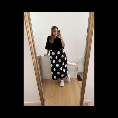 Mulher com saia preta de bolas brancas e camisola preta a tirar selfie em espelho grande com moldura dourada