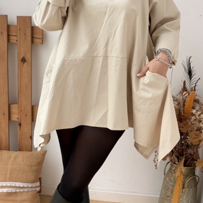 Mulher a usar vestido bege com bolso, meia preta e botas pretas com acessórios de prata, em ambiente interior decorado.