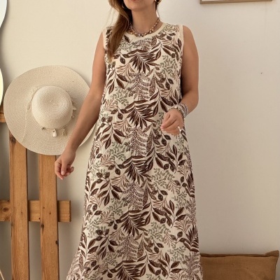 Mulher com vestido comprido floral castanho e bege, sapatos cinzentos e chapéu de palha ao lado