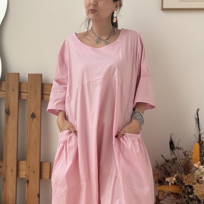 Vestido rosa claro solto com bolsos usado por mulher em ambiente interior decorado.