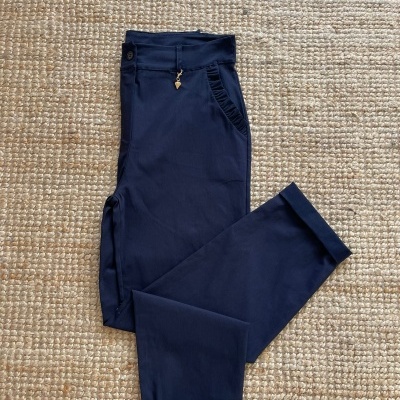 Calças azuis-escuras com bolso e detalhe dourado sobre tapete de fibras naturais