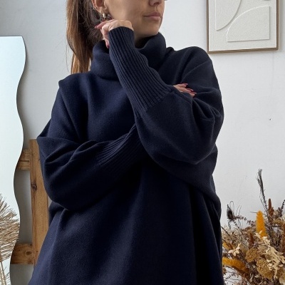 Mulher com camisola azul escura e calças xadrez num ambiente interior com parede branca e decoração