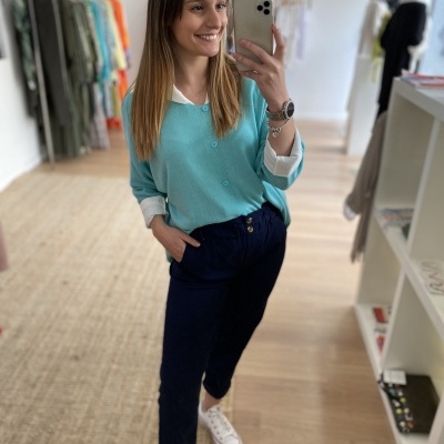 Pessoa com camisola azul clara, calças azul escuras e ténis brancos num ambiente interior moderno