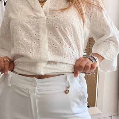 Mulher a usar camisa branca bordada e calças brancas justas com pendente dourado