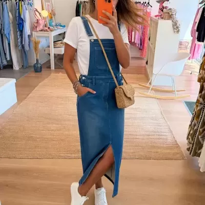 Mulher com vestido de ganga azul e t-shirt branca tirando selfie num espelho numa loja de roupa