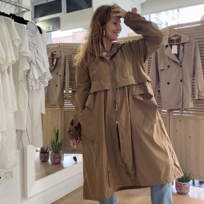 Mulher com casaco comprido bege numa loja de roupas.