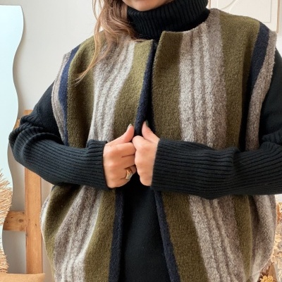 Colete de lã riscado em tons verdes e cinzentos, vestido sobre camisola preta de gola alta.