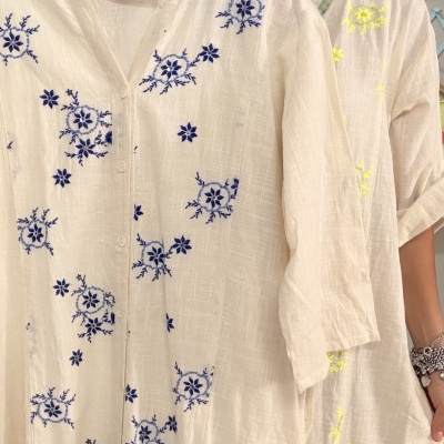 Camisa branca com bordados azuis em tecido leve segurada por mulher.