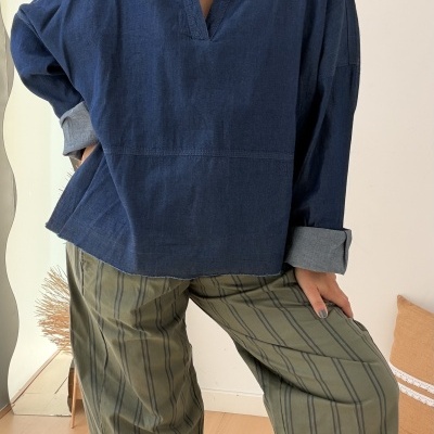 Mulher com camisa azul escura e calças verdes às riscas numa sala clara com chão de madeira