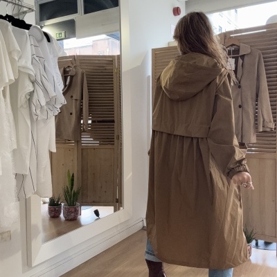 Casaco comprido castanho com capuz usado por pessoa de costas em interior