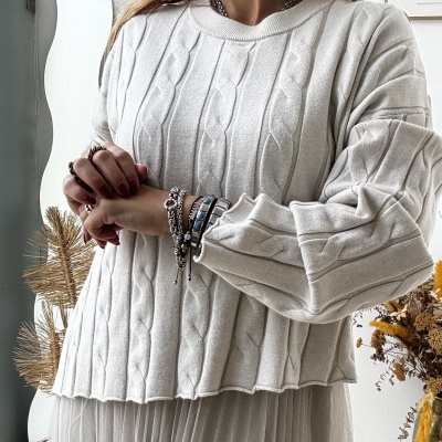 Mulher a usar camisola branca de malha com padrão de trança e saia plissada cinza clara