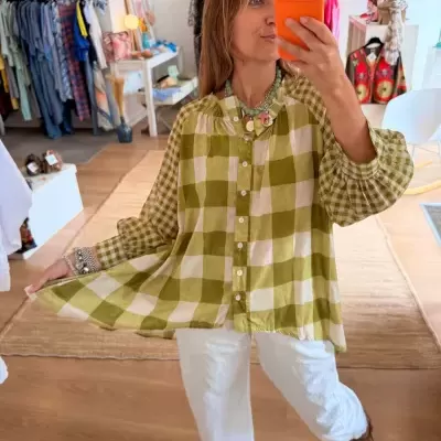Blusa xadrez verde e bege com botões e mangas bufantes em ambiente de loja de roupas