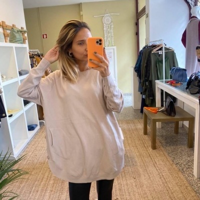 Mulher a tirar selfie com vestido camisola bege e leggings pretas numa loja de roupa