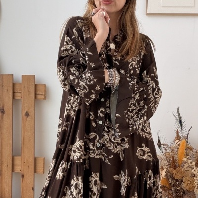 Mulher com vestido castanho estampado floral, decoração interior com vaso e quadro