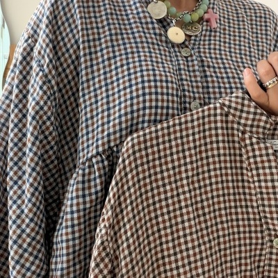 Camisas xadrez azul e castanho, castanho e bege, mulher a usá-las com colares e brincos.